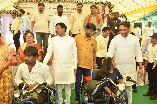 दमोह में मंच के सामने मोटराइज्ड ट्राइसाइकिल पर बैठे हितग्राहियों के साथ खड़े जनप्रतिनिधि और अधिकारी